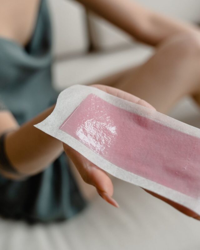 Woman holding a pink wax strip, one option for bikini line hair removal